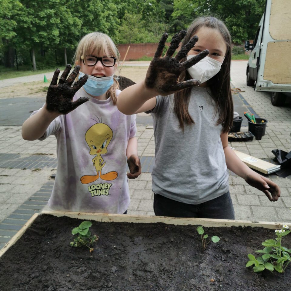 zwei Mädchen halten ihre mit Erde beschmutzen Hände hoch