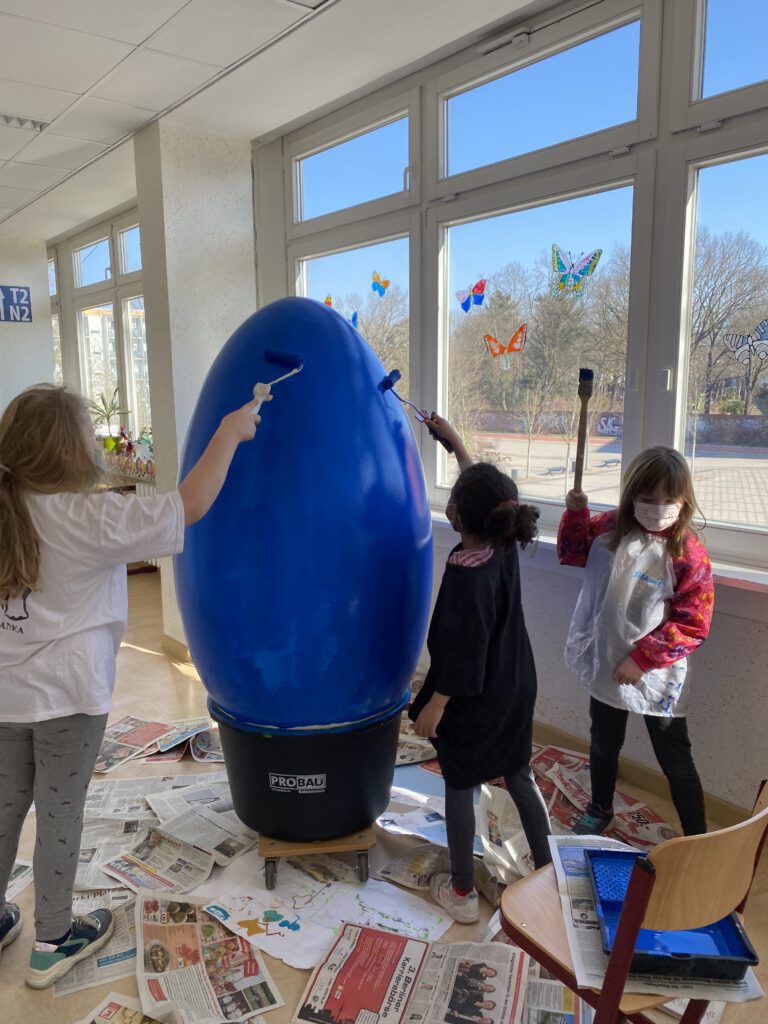 Kinder bemalen ein übergroßes Ei blau