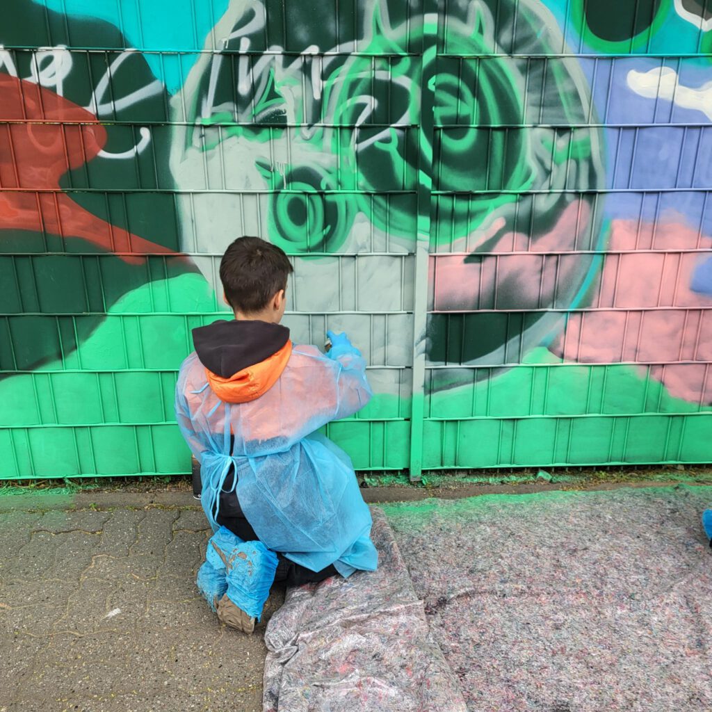 Schüler steht vor Schulzaun mit Graffitti