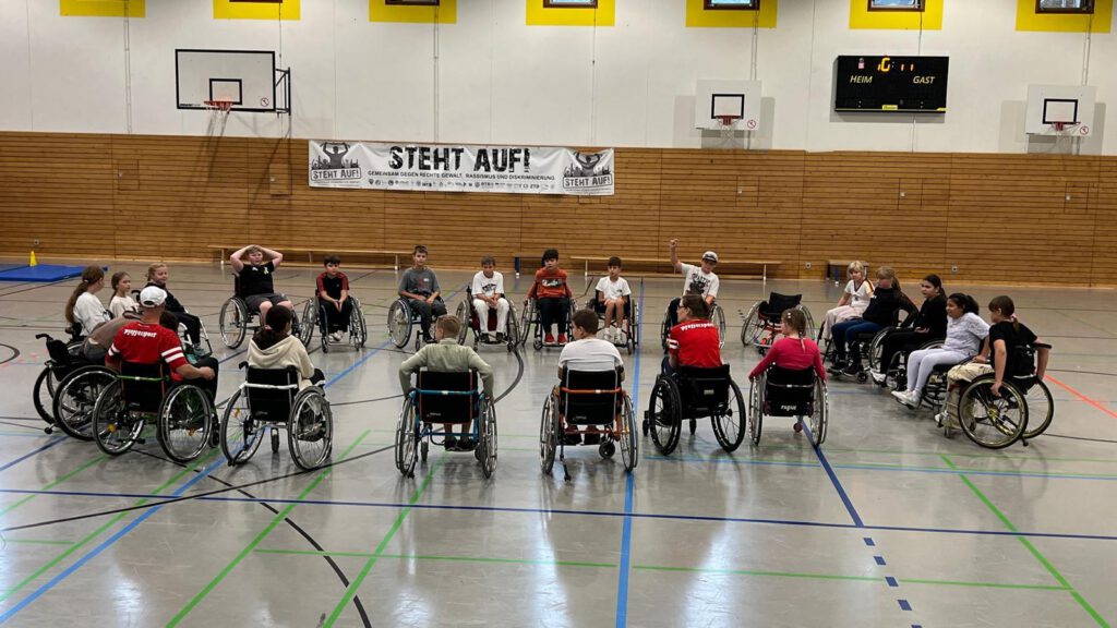 kinder der 5. Klasse im Rollstuhl in einer Turnhalle