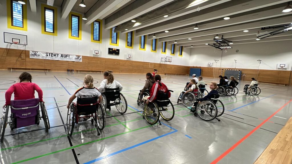 kinder der 5. Klasse im Rollstuhl in einer Turnhalle