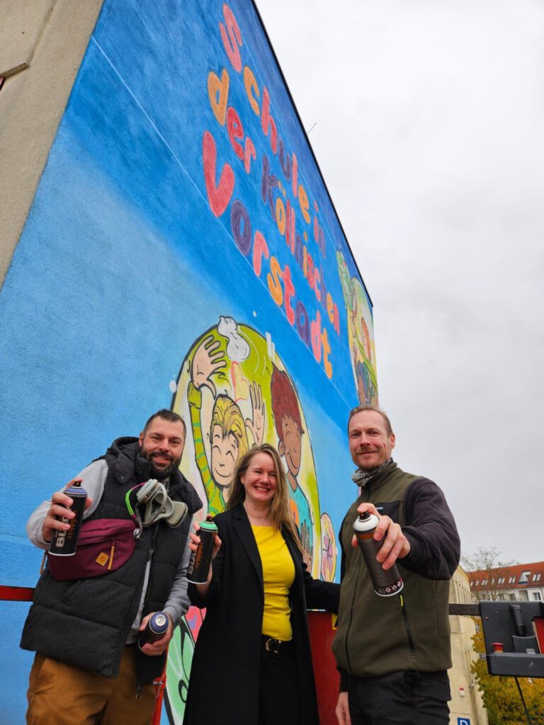 Schulleiterin und zwei Graffitikünstler stehen vor neuer Schulwand